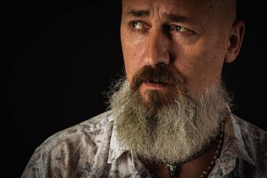 Yakın plan fotoğraf, ciddi, düşünceli, sakallı bir adamın karanlık arka planda kendine güvenen ve dramatik bir şekilde yana bakan portresi. Kavramsal erkek portresi. Alçak tuş