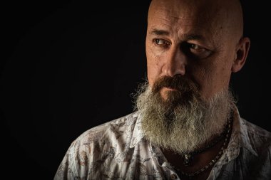 Yakın plan fotoğraf, ciddi, düşünceli, sakallı bir adamın karanlık arka planda kendine güvenen ve dramatik bir şekilde yana bakan portresi. Kavramsal erkek portresi. Alçak tuş
