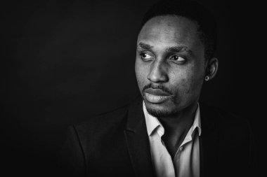 Çekici, yakışıklı, şık bir Afro-Amerikan iş adamının portresi şık bir takım elbise ve beyaz gömlek içinde, koyu bir arka planda izole edilmiş, başka yöne bakıyor. Alçakgönüllülük. Seçici odak