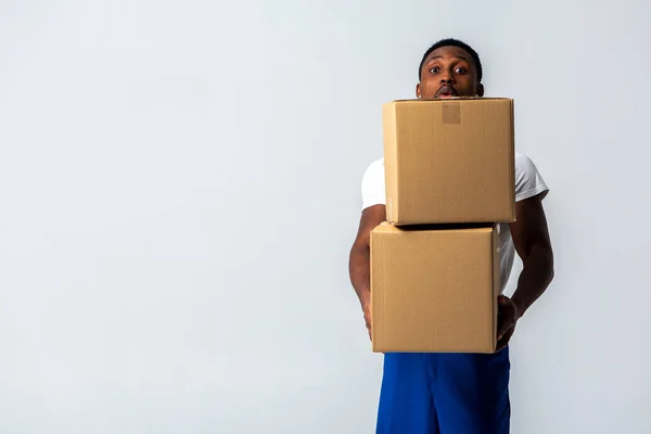 courier with a paper box, a young African American man in a blue jumpsuit and a white T-shirt holding craft paper boxes for sending. Isolated on a white background. The concept of delivery, mail, shipment, forklift