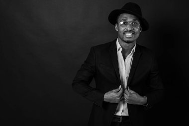 Çekici, yakışıklı, güzel, ciddi ve stil sahibi Afro-Amerikan iş adamının portresi şık takım elbiseli, beyaz gömlekli ve siyah şapkalı koyu arka planda. Alçakgönüllülük. Seçici odak