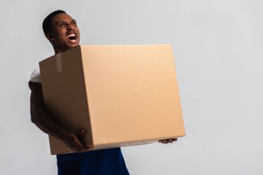 Teslimatçı elinde beyaz tişört ve elinde kutu olan mavi pantolon tutuyor. Beyaz bir arka planda izole edilmiş. Teslimat, posta, sevkiyat, yükleyici, kurye. Kutuyu kapat