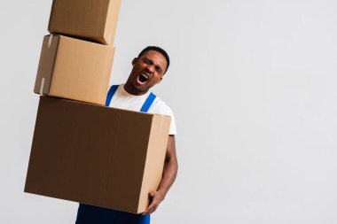 Beyaz tişört ve mavi pantolon giyen bir teslimatçı elinde kutular tutuyor. Beyaz bir arka planda izole edilmiş. Teslimat, posta, sevkiyat, yükleyici, kurye. Kutuyu kapat. İşaret dili