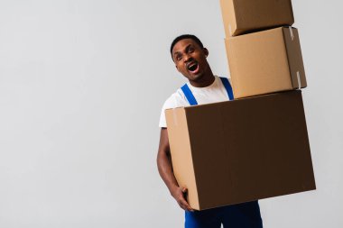 Beyaz tişört ve mavi pantolon giyen bir teslimatçı elinde kutular tutuyor. Beyaz bir arka planda izole edilmiş. Teslimat, posta, sevkiyat, yükleyici, kurye. Kutuyu kapat. İşaret dili