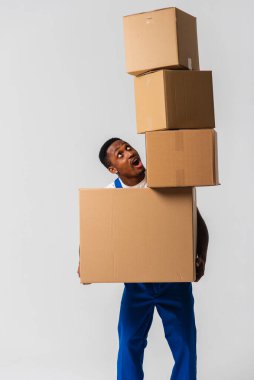 Beyaz tişört ve mavi pantolon giyen bir teslimatçı elinde kutular tutuyor. Beyaz bir arka planda izole edilmiş. Teslimat, posta, sevkiyat, yükleyici, kurye. Kutuyu kapat. İşaret dili