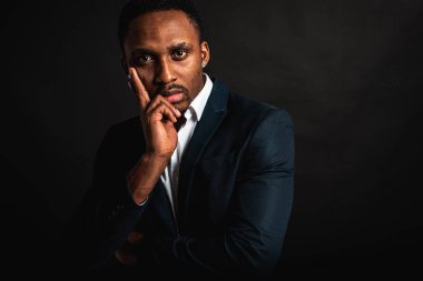 Çekici, yakışıklı, şık Afro-Amerikan iş adamının portresi şık takım elbiseli ve beyaz gömlekli koyu arkaplanda el ele tutuşan. Alçakgönüllülük. Seçici odak