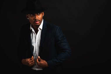 Çekici, sevimli, şık Afro-Amerikan iş adamının portresi şık takım elbiseli, beyaz gömlek ve siyah şapkalı, koyu arka planda izole edilmiş. Alçakgönüllülük. Seçici odak