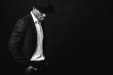 Çekici, sevimli, şık Afro-Amerikan iş adamının portresi şık takım elbiseli, beyaz gömlek ve siyah şapkalı, koyu arka planda izole edilmiş. Alçakgönüllülük. Seçici odak