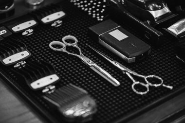 Black and white photo, selective focus, graininess, hairdressing items (nozzles for hair clippers, combs, scissors, hairdresser) are placed on the table before the haircut