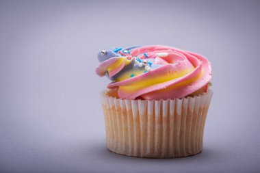 Rengarenk kremalı kekleri kapayın, renkli yıldızlı süslemeler, lezzetli ve muhteşem. Gri arkaplandaki üst görünüm. Doğum günü kavramı, kutlama, tatlı.