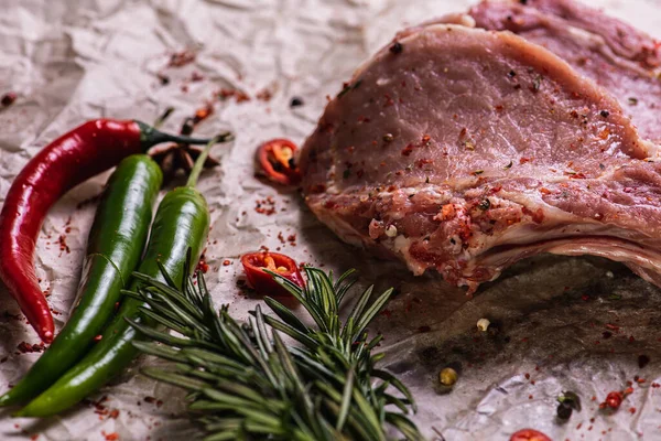 Raw fresh beef ribs steak with seasoning on a light surface, parchment, before cooking. Seasoning for meat steak with ribs for eyes rosemary, coriander, pepper. Top view, lying flat