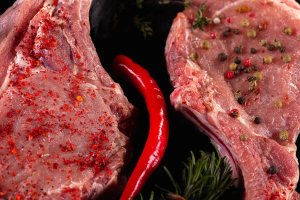 Raw fresh beef ribs steak with seasoning on a light surface, parchment, before cooking. Seasoning for meat steak with ribs for eyes rosemary, coriander, pepper. Top view, lying flat.