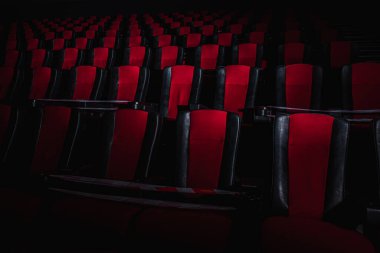 Sinema salonundaki kırmızı sandalyeler bir ışık demeti, basit bir anahtar, kısıtlayıcı bir bant ve karantina ile aydınlatılır. Seçici odaklanma. Boş sinema, COVID 19 karantinası, SARS-CoV-2, 2019-NCoV