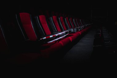 Sinema salonundaki kırmızı sandalyeler bir ışık demeti, basit bir anahtar, kısıtlayıcı bir bant ve karantina ile aydınlatılır. Seçici odaklanma. Boş sinema, COVID 19 karantinası, SARS-CoV-2, 2019-NCoV