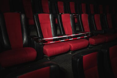 Boş sinema salonu. Sinema salonundaki koltuklar kırmızı ve siyah ışık huzmeleriyle aydınlatılır. Seçici odaklanma. Karantina, sandalyelerde kısıtlayıcı bant