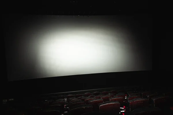 a ray of light illuminates an empty cinema. The red and black armchairs in the cinema hall are illuminated by a beam of light, a low key. Selective focus. Side view