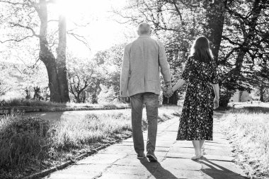 Romantik bir çift son sınıf öğrencisi, erkek ve kadın, sonbaharda, gün batımında şatonun yanındaki parkta yürüyorlar. Seçici odak