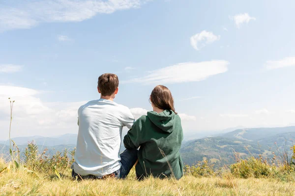 若いカップルボーイフレンドとガールフレンドは背中に座って山やロマンチックな感情や風景を見て — ストック写真