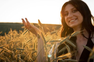 Gün batımı, yumuşak akşam renkleri, genç, güzel, duygusal esmer kız buğday tarlasında uzun saçlı, altın tarlasında. Sakinlik, ruhun huzuru.