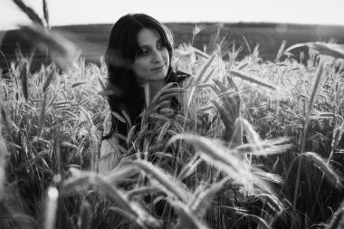 siyah ve beyaz fotoğraf, gün batımı, genç, güzel, duygusal esmer kız uzun saçlı buğday üzerinde. Sakinlik, ruhtaki huzur, duygular.