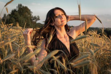 Gün batımı, yumuşak akşam renkleri, genç, güzel, duygusal esmer kız buğday tarlasında uzun saçlı, altın tarlasında. Sakinlik, ruhun huzuru.