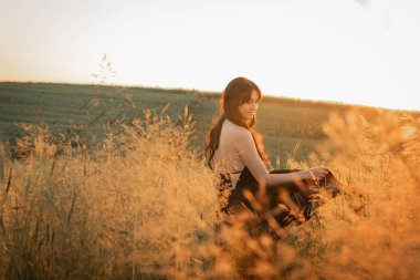 Gün batımı, yumuşak altın sarısı akşam renkleri, genç, güzel, duygusal esmer uzun siyah uzun elbiseli kız altın buğday tarlasında. Ruhun rahatlığı, neşe, doğa