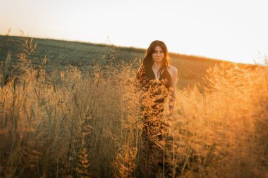 Gün batımı, yumuşak altın sarısı akşam renkleri, genç, güzel, duygusal esmer uzun siyah uzun elbiseli kız altın buğday tarlasında. Ruhun rahatlığı, neşe, doğa