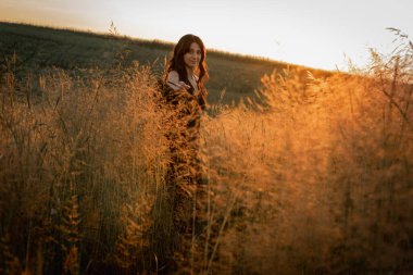 Gün batımı, yumuşak altın sarısı akşam renkleri, genç, güzel, duygusal esmer uzun siyah uzun elbiseli kız altın buğday tarlasında. Ruhun rahatlığı, neşe, doğa