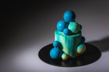 Mavi doğum günü pastası, üzerinde beyaz ve mavi çikolata topları ile bir fincan mavi kahve, gri arka planda. Gölge ve ışık, karşıtlık