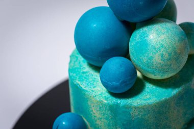 Mavi doğum günü pastası, üzerinde beyaz ve mavi çikolata topları ile bir fincan mavi kahve, gri arka planda. Gölge ve ışık, karşıtlık