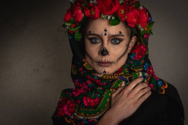 Kafasında çiçek çelengi olan Ölüler Günü için makyaj yapan genç bir kız. Çiçekli bir dantel takıyor. Düz görünüyor, gri bir arka planda izole edilmiş. Cadılar Bayramı ya da La Calavera Katrina konsepti.