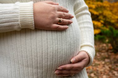 Müstakbel bir çiftin ellerine yakın çekim: anne hamile karnını kucaklarken, baba nazikçe bir çift küçük örülmüş bebek paçası tutuyor.
