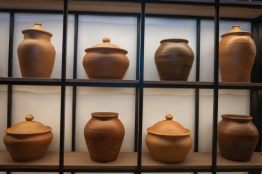 Kara metal çerçeveli ahşap raflarda sergilenen el yapımı kahverengi çömlek koleksiyonu. Rustik seramik mutfak geriışıklandırmalı modern iç mekan. Çömlek dekoru