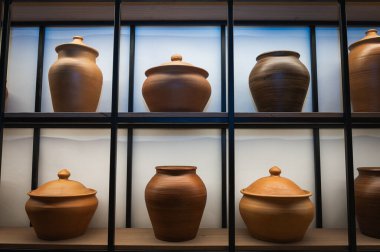 Kara metal çerçeveli ahşap raflarda sergilenen el yapımı kahverengi çömlek koleksiyonu. Rustik seramik mutfak geriışıklandırmalı modern iç mekan. Çömlek dekoru