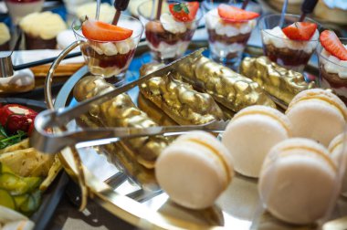 Şatafatlı altın ekler, beyaz badem kurabiyeleri ve çilekli tatlı kupaları bir düğün ya da ziyafet için gurme büfesinde maşayla servis edilir.