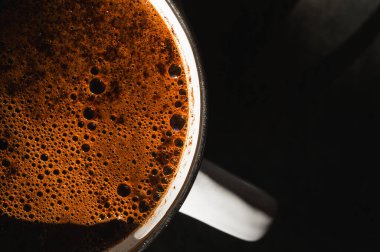 Kahverengi köpüklü kahve fincanının makro üst görüntüsü. Koyu arkaplanda taze sıcak espresso krema dokusu. Sabah enerji içeceği ve kafein aroması konsepti
