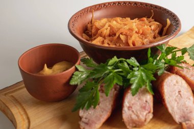 Ahşap tahtada ızgara sosis, hardal ve maydanoz ile birlikte kilden kasede geleneksel haşlanmış lahana. Kırsal Doğu Avrupa mutfağında haşlanmış lahana turşusu.