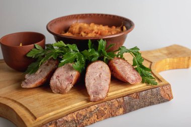 Ahşap tahtada ızgara sosis, hardal ve maydanoz ile birlikte kilden kasede geleneksel haşlanmış lahana. Kırsal Doğu Avrupa mutfağında haşlanmış lahana turşusu.