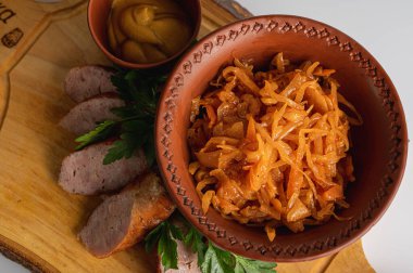 Ahşap tahtada ızgara sosis, hardal ve maydanoz ile birlikte kilden kasede geleneksel haşlanmış lahana. Kırsal Doğu Avrupa mutfağında haşlanmış lahana turşusu.