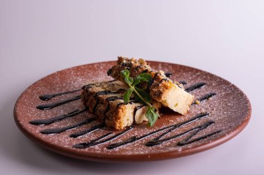 Makro katmanlı ballı kek dilimleri çikolata soslu ve taze naneli. Ekmek kırıntısı desenli gurme tatlı ve kil tabakta pudra şekeri. Tatlı pasta konsepti