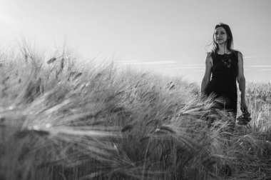 Buğday tarlasında siyah elbiseli bir kadının dramatik siyah beyaz portresi. Bulanık ön plan, karamsar ışıklandırma ve yüksek kontrastlı sanatsal çekim