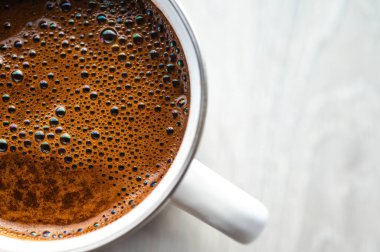 Gri ahşap bir zeminde beyaz bir diş minesi kupasında köpüklü taze siyah kahvenin en üst görüntüsü. Minimalist kırsal sabah kahve molası konsepti. Doğal ışık ve kopyalama alanı