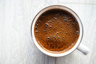 Gri ahşap bir zeminde beyaz bir diş minesi kupasında köpüklü taze siyah kahvenin en üst görüntüsü. Minimalist kırsal sabah kahve molası konsepti. Doğal ışık ve kopyalama alanı