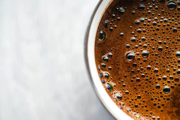 Gri ahşap bir zeminde beyaz bir diş minesi kupasında köpüklü taze siyah kahvenin en üst görüntüsü. Minimalist kırsal sabah kahve molası konsepti. Doğal ışık ve kopyalama alanı