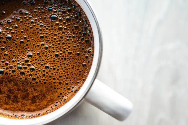 Gri ahşap bir zeminde beyaz bir diş minesi kupasında köpüklü taze siyah kahvenin en üst görüntüsü. Minimalist kırsal sabah kahve molası konsepti. Doğal ışık ve kopyalama alanı