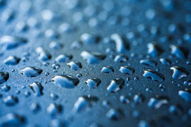 Koyu mavi desenli yüzeydeki temiz su damlacıklarının makro görüntüsü. Derin mavi renkleri ve yüksek kontrastı olan soyut sıvı deseni. Teknoloji ve doğa geçmişi için mükemmel.