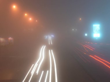 Yanan sokak lambaları ve otoyol raylarıyla sisli gece sokağı manzarası
