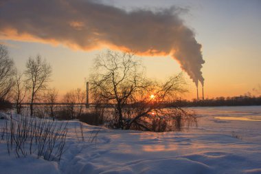 Donmuş bir nehir, tüten bir pipo ve batan bir güneş olan kış manzarası.