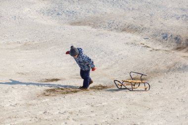 Kış giysileri içinde kızaklı küçük bir çocuk.