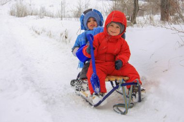 two small boys in winter clothes are sitting on a sleigh